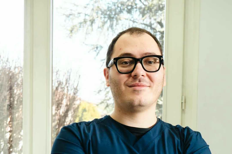 Il Dott. Andrea Martinelli sorride accanto alla poltrona, davanti alla portafinestra dello studio